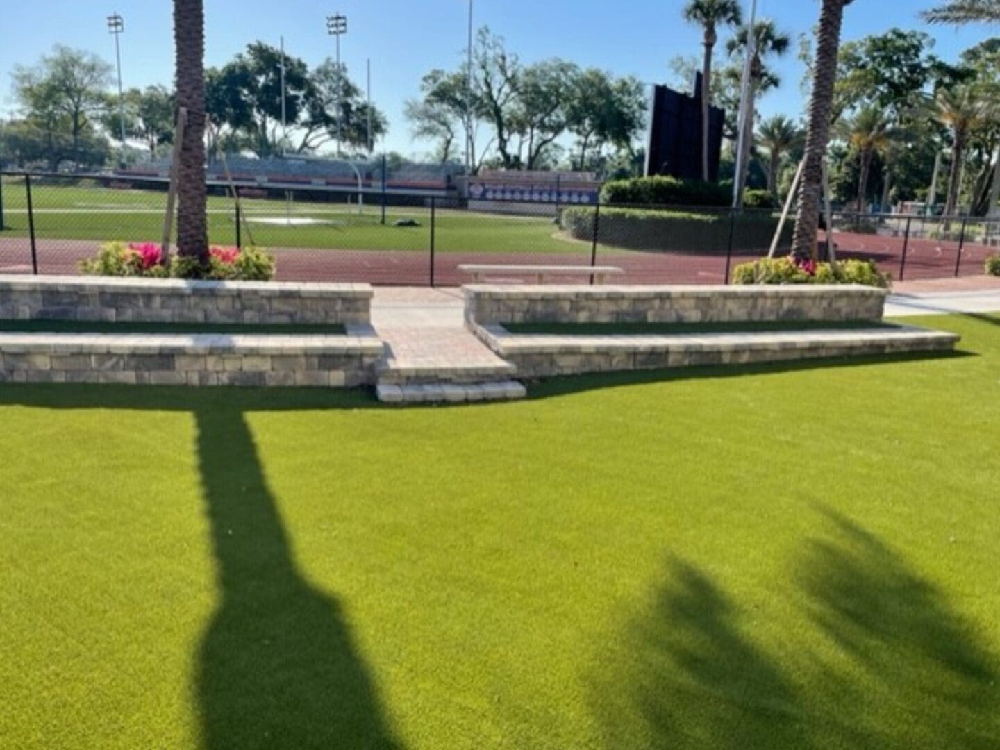 A well-manicured artificial grass area in North East Florida with a stepped retaining wall and palm trees casting long shadows.