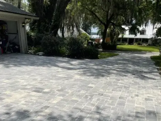 Paved residential driveway with a garage on the left, surrounded by trees and landscaping.