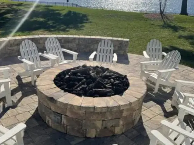 Outdoor fire pit with surrounding chairs on a patio by the water.