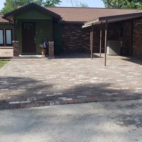 Brick-paved driveway leading to a single-story house with a green door and carport in North East Florida.