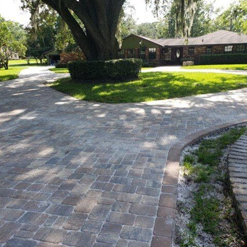 Paved residential driveway with a curved design leading to a house in North East Florida, featuring a lawn and trees.